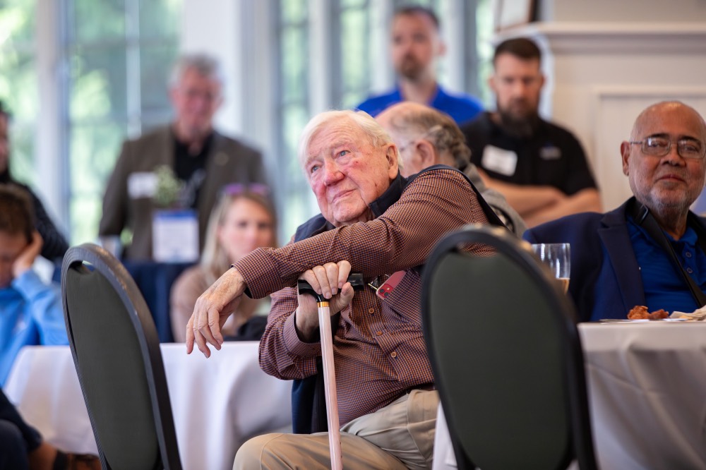 President Emeritus Don Lubbers listens to rowing speech while rest arm on cane